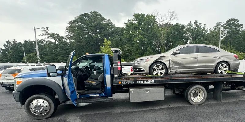 The whole truck in a parking lot with a silver sedan strapped on the bed