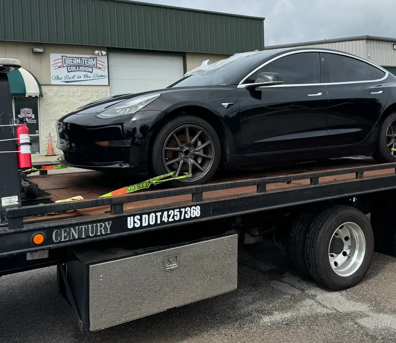 A black Tesla Model 3 strapped down on the flatbed, USDOT number lettered on the bed