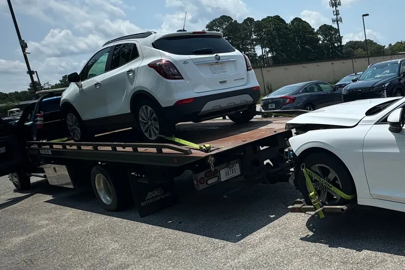 Two cars at once: a white SUV up on the flatbed and a white sedan strapped to its tail with yellow straps